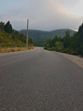 Pürüzsüz bir asfalt yol engebeli dağ yamaçlarında kara kara düşünen, bulutlu bir gökyüzünün altında ilerler. Bulutlar sivri tepeler boyunca toplanır, Rif dağlarındaki yıpranmış kayaların üzerine gölgeler düşer.