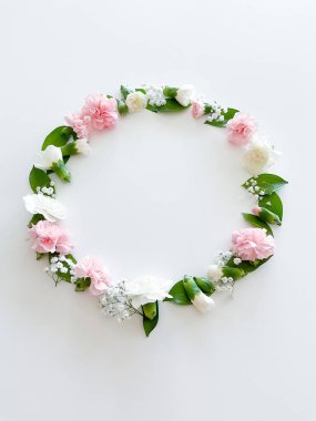 Pembe ve beyaz karanfillerden oluşan yuvarlak bir çerçeve, yeşil yapraklar, beyaz arka planda çingene. Düz yerde, üst tarafta. Bahar arka planı. Düğün, kartlar ve davetiyeler için uygun