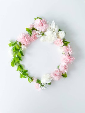Pembe ve beyaz karanfillerden oluşan yuvarlak bir çerçeve, yeşil yapraklar, beyaz arka planda çingene. Düz yerde, üst tarafta. Bahar arka planı. Düğün, kartlar ve davetiyeler için uygun
