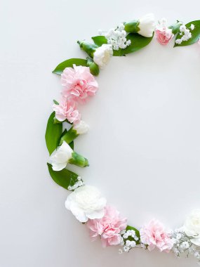Pembe ve beyaz karanfillerden oluşan yuvarlak bir çerçeve, yeşil yapraklar, beyaz arka planda çingene. Düz yerde, üst tarafta. Bahar arka planı. Düğün, kartlar ve davetiyeler için uygun