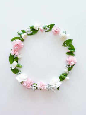 Pembe ve beyaz karanfillerden oluşan yuvarlak bir çerçeve, yeşil yapraklar, beyaz arka planda çingene. Düz yerde, üst tarafta. Bahar arka planı. Düğün, kartlar ve davetiyeler için uygun