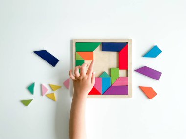 Childs el, beyaz arka planda çok renkli ahşap mozaik koleksiyonu yapıyor. Çocuk renkli bir tangram çözüyor. Beyaz arkaplanda renkli geometrik şekillerin karesi.