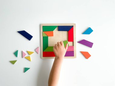 Childs el, beyaz arka planda çok renkli ahşap mozaik koleksiyonu yapıyor. Çocuk renkli bir tangram çözüyor. Beyaz arkaplanda renkli geometrik şekillerin karesi.