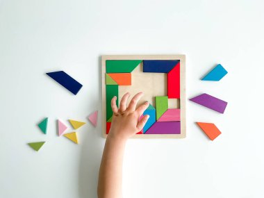 Childs el, beyaz arka planda çok renkli ahşap mozaik koleksiyonu yapıyor. Çocuk renkli bir tangram çözüyor. Beyaz arkaplanda renkli geometrik şekillerin karesi.
