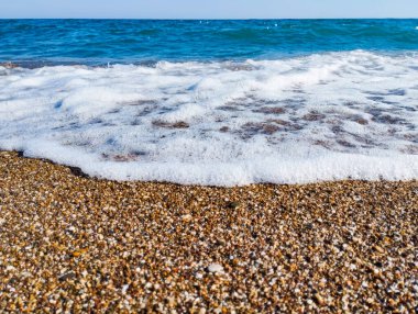 Çakıl taşlı plajı ve deniz köpüklü mavi dalgaları olan güzel bir deniz arka planı. Yüksek kalite fotoğraf