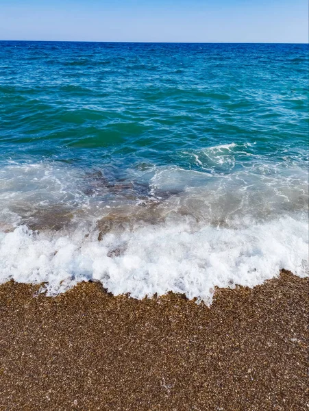 Çakıl taşlı plajı ve deniz köpüklü mavi dalgaları olan güzel bir deniz arka planı. Yüksek kalite fotoğraf