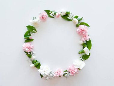 Pembe ve beyaz karanfillerden oluşan yuvarlak bir çerçeve, yeşil yapraklar, beyaz arka planda çingene. Düz yerde, üst tarafta. Bahar arka planı. Düğün, kartlar ve davetiyeler için uygun
