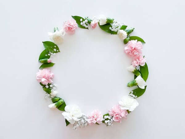 Round frame of pink and white carnations, green leaves, gypsophila on a white background. Flat lay, top view. Spring background. Suitable for wedding, cards and invitations