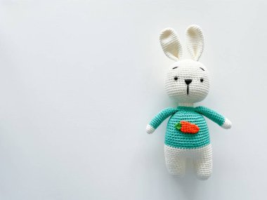 Yumuşak beyaz örgü ören tavşan. Beyaz bir arka planda. El yapımı çocuk oyuncağı. Göğsünde havuç olan büyük, peluş bir tavşan. Mutlu çocukluk kavramı