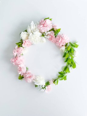 Pembe ve beyaz karanfillerden oluşan yuvarlak bir çerçeve, yeşil yapraklar, beyaz arka planda çingene. Düz yerde, üst tarafta. Bahar arka planı. Düğün, kartlar ve davetiyeler için uygun