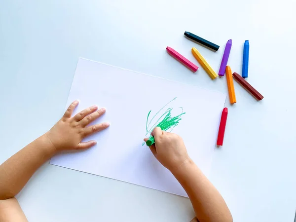Küçük çocuk beyaz masaya pastel boya kalemleriyle resim çiziyor. Yüksek kalite fotoğraf
