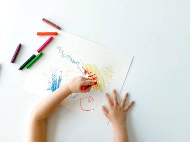 Küçük çocuk beyaz masaya pastel boya kalemleriyle resim çiziyor. Yüksek kalite fotoğraf