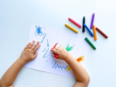 Küçük çocuk beyaz masaya pastel boya kalemleriyle resim çiziyor. Yüksek kalite fotoğraf