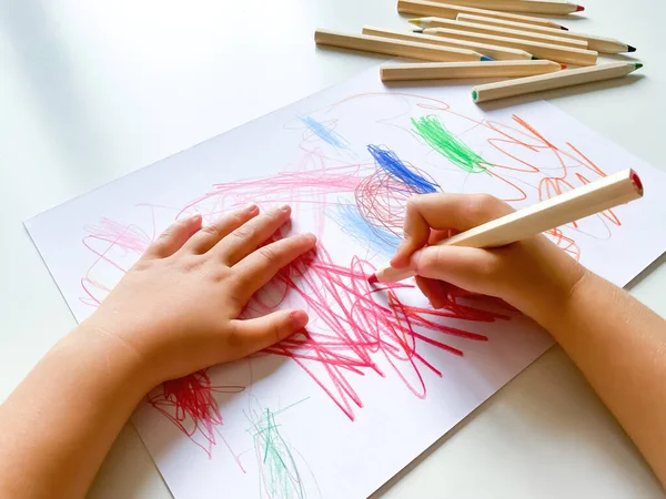 Küçük çocuk beyaz masanın üzerine renkli kalemlerle kağıt çizer. Yüksek kalite fotoğraf