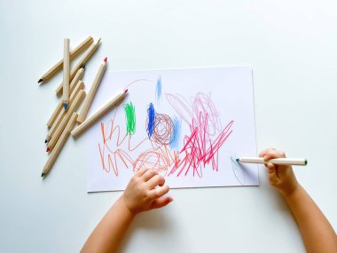 Küçük çocuk beyaz masanın üzerine renkli kalemlerle kağıt çizer. Yüksek kalite fotoğraf