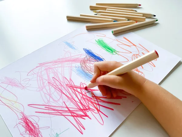 small child draws with colored pencils on paper on white table. High quality photo
