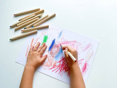 Küçük çocuk beyaz masanın üzerine renkli kalemlerle kağıt çizer. Yüksek kalite fotoğraf