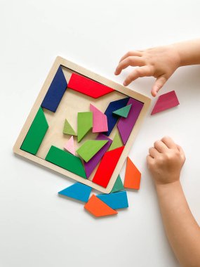 Childs el, beyaz arka planda çok renkli ahşap mozaik koleksiyonu yapıyor. Çocuk renkli bir tangram çözüyor. Beyaz arkaplanda renkli geometrik şekillerin karesi.