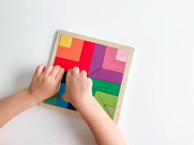 Childs el, beyaz arka planda çok renkli ahşap mozaik koleksiyonu yapıyor. Çocuk renkli bir tangram çözüyor. Beyaz arkaplanda renkli geometrik şekillerin karesi.