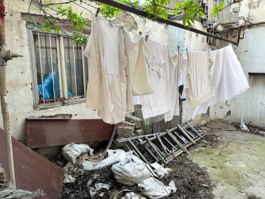 Aşırı büyümüş yapraklar, kırık mobilyalar ve çöplerle harap olmuş şehir bahçesinde, bakımsızlığı ve yoksul mahalledeki günlük hayatı ve yoksulluğu tasvir eden çamaşırhaneler asılı duruyor. Yüksek kalite fotoğraf