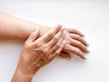 Beyaz manikürlü elleri olan orta yaşlı bir kadın beyaz arka planda nazikçe birbirine dokunuyor. Düz kompozisyon. Cilt bakımı ve el bakımı ya da anne sevgisi kavramı. Yüksek kalite fotoğraf