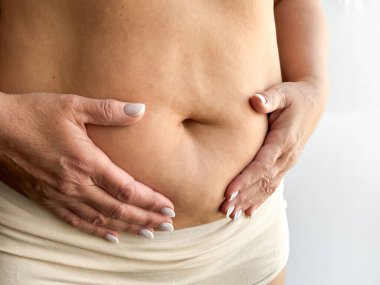 Beyaz arka planda bej rengi iç çamaşırlarıyla elleri nazikçe dokunarak göbeğini kapat. Annelik ve annelik kavramı. Sağlık sigortası, doğum sonrası bakım, sağlık için tasarım. Yüksek kalite fotoğraf