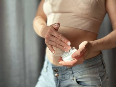 Kavanozdan krema alan kadına yaklaş. Seçici olarak ellere ve kozmetik kreme odaklan. Tarafsız arka planda koyu ışık. Cilt bakımı, hidrasyon, kendini sevme ve kendine bakma kavramı. Yaşam tarzı fotoğrafı..