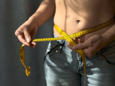 Kotlu, belini sarı şeritle ölçen yüzsüz kadının yakın çekimi. Kilo kaybı, zindelik ve sağlık için vücut ölçüm konsepti. Yaşam tarzı fotoğrafı. Yüksek kalite fotoğraf