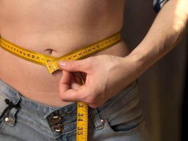 Kotlu, belini sarı şeritle ölçen yüzsüz kadının yakın çekimi. Kilo kaybı, zindelik ve sağlık için vücut ölçüm konsepti. Yaşam tarzı fotoğrafı. Yüksek kalite fotoğraf