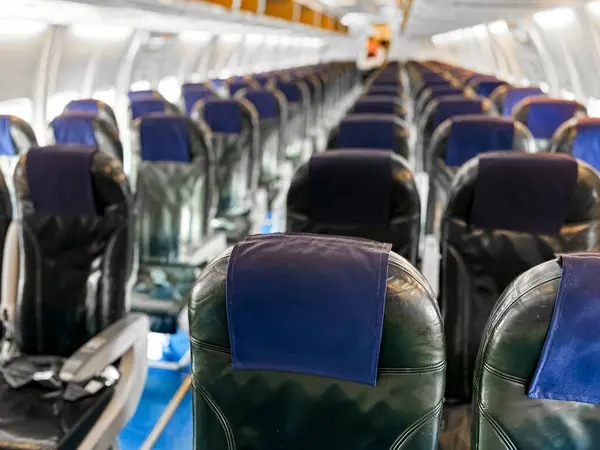 stock image Interior view of empty airplane cabin with rows of black leather seats and blue headrest covers, illuminated by overhead lights, showing aisle running down middle, windows on both sides. High quality