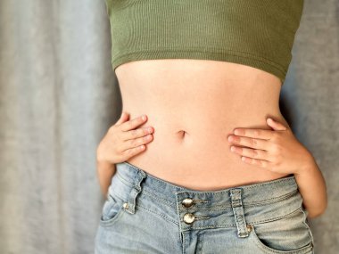 Kotlu, yeşil bluzlu, elleri belinde bir kadın resmi. Aile bağı, annelik, doğum sonrası iyileşme ve şefkat kavramı. Tarafsız bir arkaplan. Yüksek kalite fotoğraf