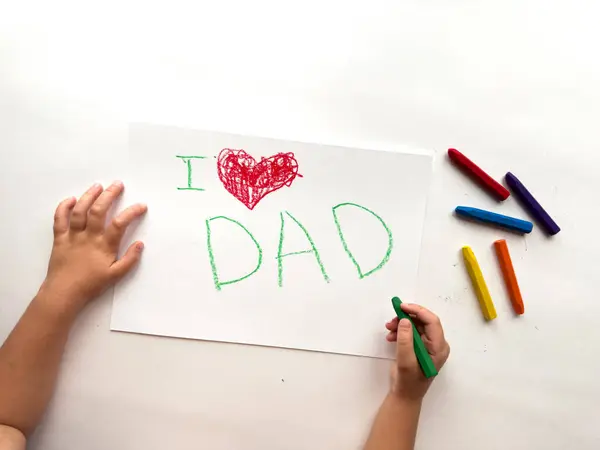 Childs beyaz kağıda renkli pastel boyaları ve baba mesajını seviyor..