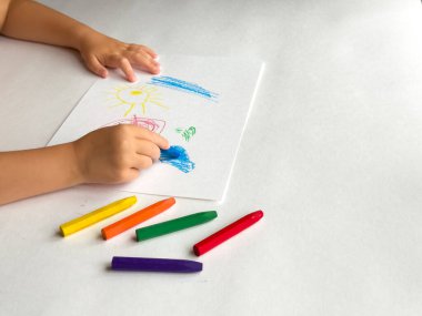 Beyaz kağıda boya kalemleri çizen çocuk renkli sanat eserleri yaratıyor.