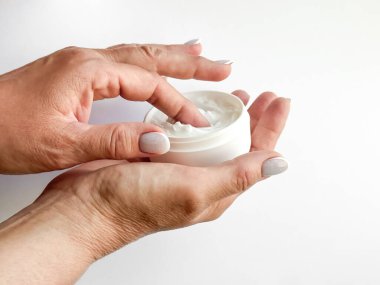 Close up of middle age woman hands holding container of cream and dipping finger on white background. Skincare and moisturizing concept. For healthcare, wellness, and self care poster. High quality clipart