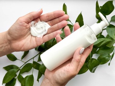 Close up of middle age woman hand holding white lotion bottle with green leaves on white background. Skincare and natural beauty concept. Healthcare, wellness, and organic product poster. High quality clipart