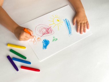 Beyaz kağıda renkli boya kalemleri çizen çocuk..