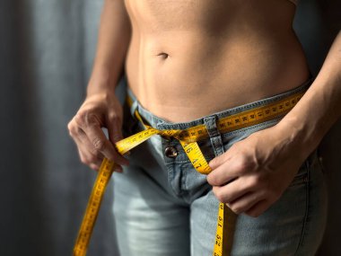 Tarafsız arka planda kemer yerine sarı şeritli kot pantolonlu çıplak kadının çıplak gövdesini kapat. Kilo kaybı, zindelik ya da vücut ölçüsü konsepti. Yaşam tarzı fotoğrafı. Yüksek kalite