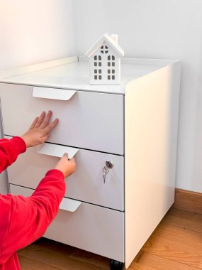 Kırmızılı çocuk küçük ev süsleriyle beyaz dolap çekmecesine uzanıyor..
