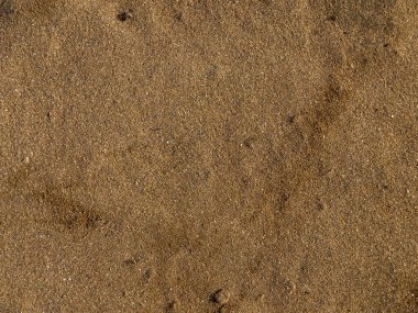 Küçük çakıl taşları ve ince desenleri olan kahverengi kumlu plaj yüzeyi.