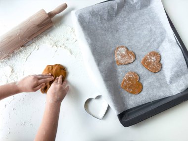 Çocuk merdane ve kurabiye keskisiyle yemek tepsisinde kalp şeklinde kurabiyeler yapıyor..