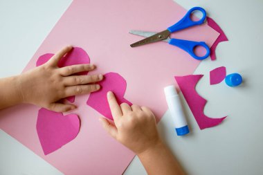 Çocuk pembe kağıt ve mavi makasla kalp şeklinde el sanatları yapıyor..