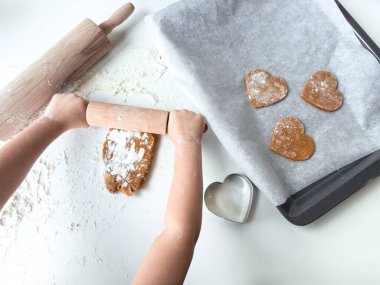 Çocuk merdane ve fırın tepsisiyle kalp şeklinde kurabiyeler yapıyor..