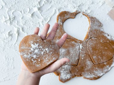 Heart shaped cookie dough being prepared on floured surface. clipart