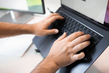 Klavyede dizüstü bilgisayarı olan ve arka planda monitör kullanan erkeklerin ellerini kapat.