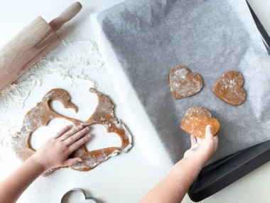 Un kaplı yüzeyde kalp şeklinde hamurla kurabiye pişiren çocuk..