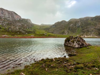 Sakin dağ gölü. Kaya ve yeşil tepeler bulutlu gökyüzü altında..