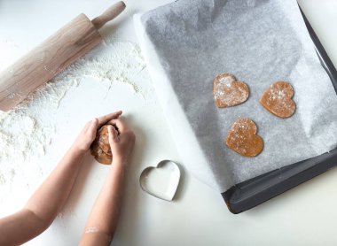 Çocuk kalp şeklinde kurabiyeler pişiriyor hamur ve oklava ile un kaplı yüzeyde.