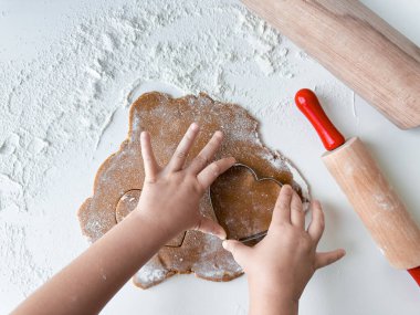 Yuvarlak iğnelerle kalp şeklinde kurabiye hamuru kesen çocuk..