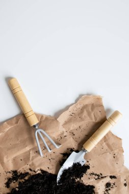 Kahverengi kağıt ve toprak zemin üzerinde ahşap saplı bahçe araçları.