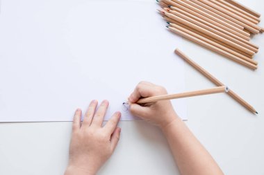 Beyaz kağıt yüzeyinde kurşun kalemlerle çizim yapan çocuk.